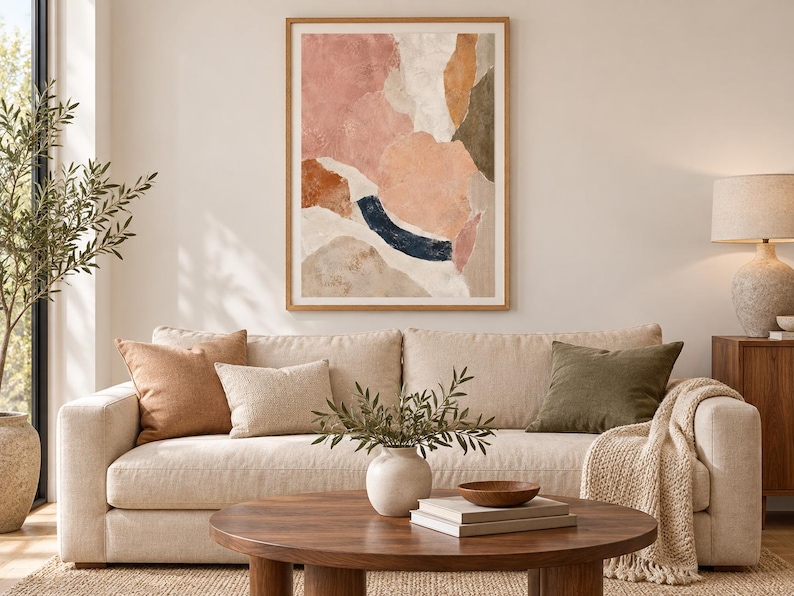 May include: A framed abstract wall art print featuring organic shapes in muted tones of dusty pink, terracotta, cream, olive green, and a dark navy blue arc, displayed in a light wood frame with a white mat border on a neutral-colored wall.
