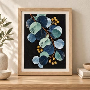 May include: A framed wall art print featuring a botanical illustration of a eucalyptus branch with round leaves in shades of navy blue, teal, and light green against a solid black background, accented by small golden seed pods on brown stems.