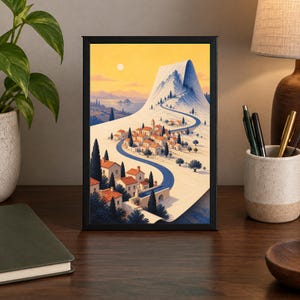May include: A framed vertical art print depicting a Mediterranean-style village with terracotta-roofed buildings nestled at the base of a large, snow-capped mountain. A winding blue road leads through the town toward the peak under a golden sky.