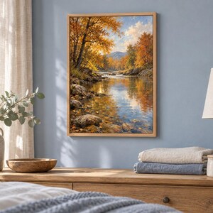 K&ouml;nnte beinhalten: Ein rechteckiges gerahmtes Wandbild, das eine ruhige Herbstlandschaft mit einem flie&szlig;enden Fluss, felsigen Ufern und leuchtend orangefarbenen sowie gelben B&auml;umen unter einem hellblauen Himmel in einem realistischen Malstil zeigt.