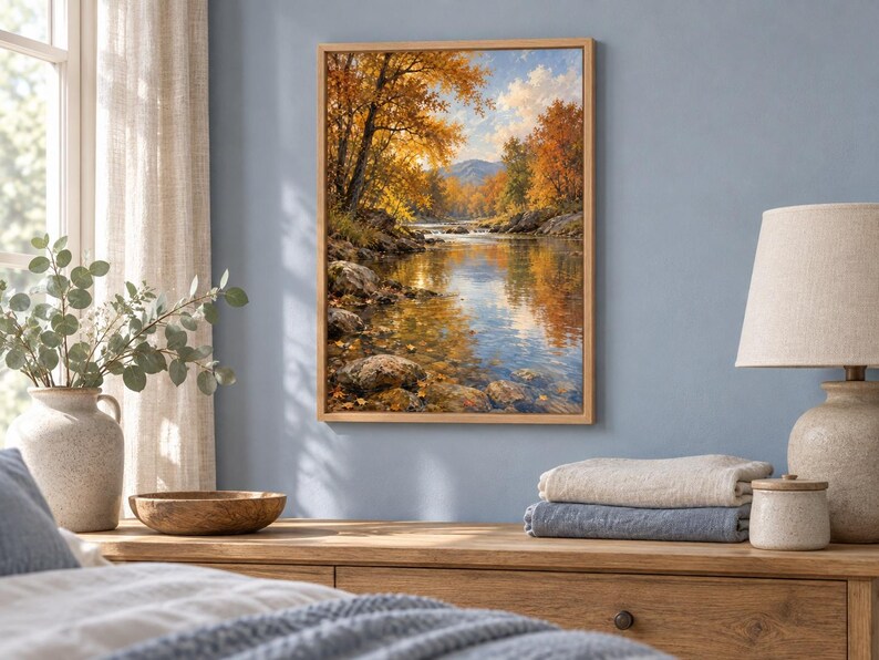 K&ouml;nnte beinhalten: Ein rechteckiges gerahmtes Wandbild, das eine ruhige Herbstlandschaft mit einem flie&szlig;enden Fluss, felsigen Ufern und leuchtend orangefarbenen sowie gelben B&auml;umen unter einem hellblauen Himmel in einem realistischen Malstil zeigt.