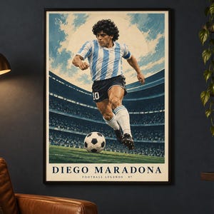 K&ouml;nnte beinhalten: Ein gerahmtes vertikales Poster mit einer stilisierten Illustration eines Fu&szlig;ballspielers in einem hellblau-wei&szlig; gestreiften Trikot und schwarzen Shorts, der einen Fu&szlig;ball auf einem Spielfeld tritt. Der Text DIEGO MARADONA FOOTBALL LEGENDS 07 steht unten.