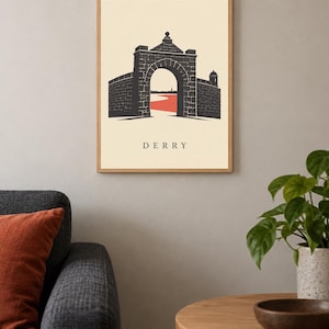 May include: A framed wall art print featuring a graphic illustration of a stone archway and city walls. The design uses a cream background, black stone textures, and a red path leading through the gate. The word DERRY is printed in black below.