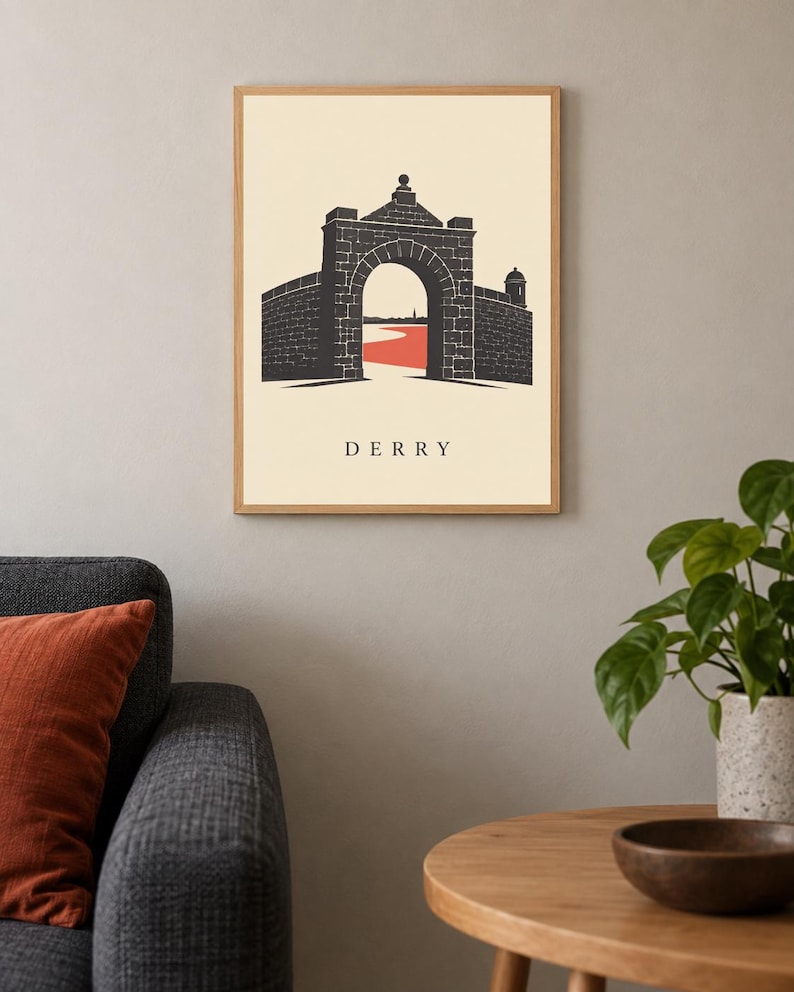 May include: A framed wall art print featuring a graphic illustration of a stone archway and city walls. The design uses a cream background, black stone textures, and a red path leading through the gate. The word DERRY is printed in black below.