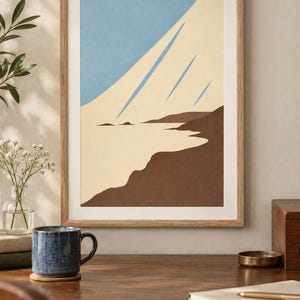 May include: A framed wall art print featuring a stylized coastal landscape with a light blue sky, a cream-colored expanse representing sand or water, and dark brown landforms. The artwork is enclosed in a simple light wood frame.