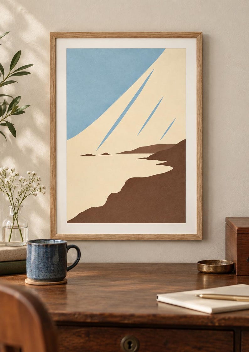 May include: A framed wall art print featuring a stylized coastal landscape with a light blue sky, a cream-colored expanse representing sand or water, and dark brown landforms. The artwork is enclosed in a simple light wood frame.