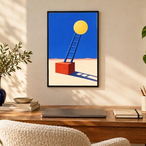 May include: A framed wall art print featuring a surrealist illustration of a blue ladder leaning against a large yellow circle, set atop a red cube on a beige ground against a solid blue sky, casting a long, dark shadow across the surface.