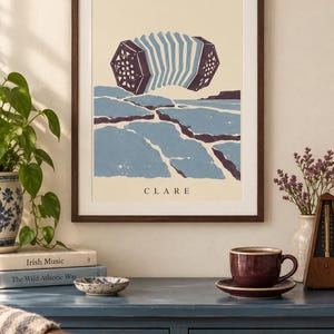 May include: A framed art print featuring a stylized illustration of a concertina floating above a blue and cream landscape. The word CLARE is printed in black at the bottom center of the cream-colored background within the dark wood frame.