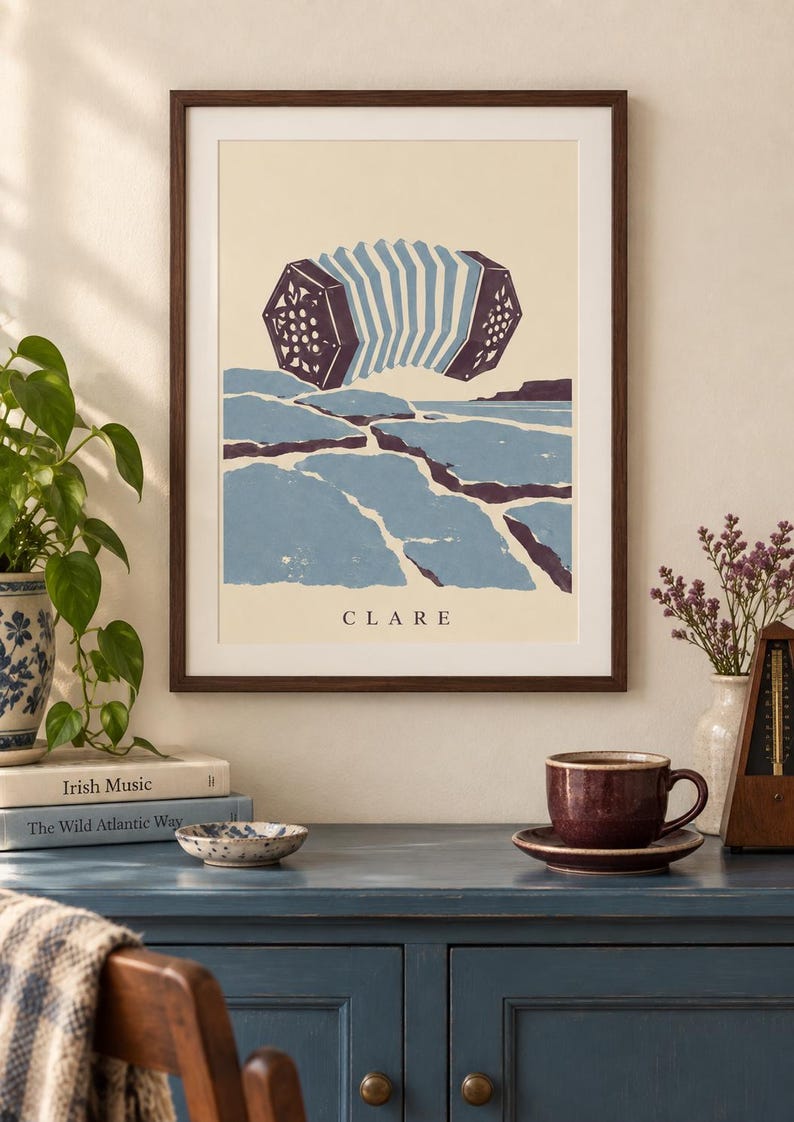 May include: A framed art print featuring a stylized illustration of a concertina floating above a blue and cream landscape. The word CLARE is printed in black at the bottom center of the cream-colored background within the dark wood frame.