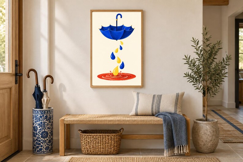 Pu&ograve; includere: Una stampa artistica da parete incorniciata che raffigura un ombrello blu sospeso in aria, con gocce di pioggia gialle e blu che cadono in una pozzanghera circolare rossa. L'opera &egrave; esposta in una cornice di legno chiaro su una parete neutra.