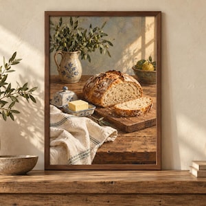 Peut inclure: Une impression d'art murale encadr&eacute;e repr&eacute;sentant une nature morte rustique sur une table en bois. L'image montre une miche de pain au levain, une tranche de pain, un beurrier avec un carr&eacute; de beurre jaune, un pichet en c&eacute;ramique et un bol.