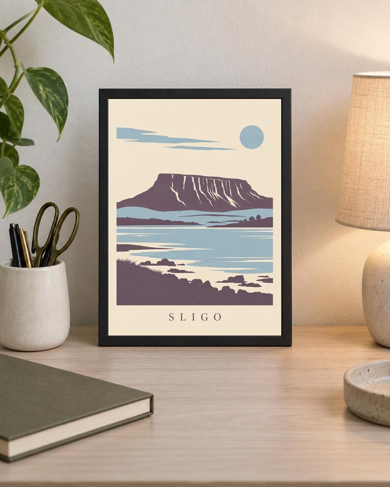 May include: A framed art print featuring a stylized landscape illustration of Sligo with a prominent flat-topped mountain, a body of water, and a pale blue sun against a cream background. The word SLIGO is printed in black at the bottom center.