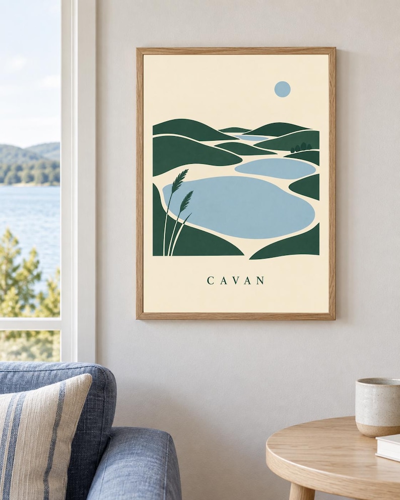 May include: A framed wall art print featuring a stylized landscape illustration of green rolling hills, light blue bodies of water, and a small blue circle representing the sun. The word CAVAN is printed in black capital letters at the bottom.