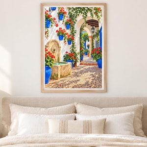 May include: A framed wall art print depicting a sunlit Mediterranean courtyard with a stone fountain, vibrant red geraniums in bright blue pots mounted on white walls, climbing green ivy, and a cobblestone path leading through an arched doorway.