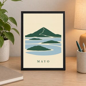 Pu&ograve; includere: Una stampa rettangolare incorniciata che presenta un'illustrazione paesaggistica stilizzata di una montagna e isole verde scuro su uno sfondo d'acqua azzurro in un campo color crema, con la parola MAYO stampata in verde scuro in basso.
