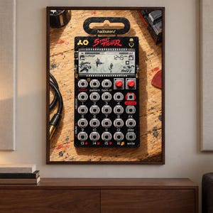 May include: A black Street Fighter edition pocket synthesiser featuring a digital display with character graphics, sixteen numbered circular buttons, two red knobs, and various control labels. The device is mounted in a dark frame.