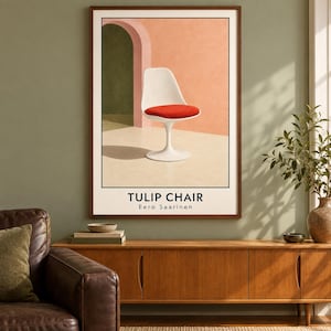 May include: A framed wall art print featuring a white tulip chair with a red seat cushion set against a peach wall and an arched doorway. The text TULIP CHAIR and Eero Saarinen is printed in black at the bottom of the white-bordered poster.