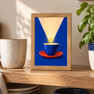 Puede incluir: Un marco de madera rectangular que contiene una impresi&oacute;n de una taza de caf&eacute; azul sobre un platillo rojo. Sobre la taza, una fuente de luz circular amarilla emite un haz triangular contra un fondo azul s&oacute;lido, creando una composici&oacute;n gr&aacute;fica.
