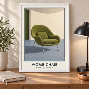 May include: A framed wall art print featuring a green Womb Chair designed by Eero Saarinen. The illustration shows the chair with thin metal legs against a cream and green background. The text WOMB CHAIR and Eero Saarinen appears below.