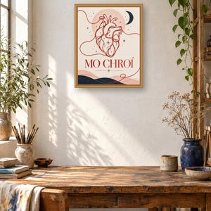 May include: A rectangular wall art print in a gold frame featuring a red line-art anatomical heart illustration, a dark blue crescent moon, and the text MO CHRO&Iacute; centered above dark blue abstract hills on a light cream background.