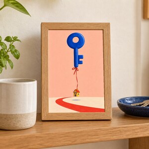 May include: A rectangular wooden frame containing a print of a blue key floating like a balloon, tied by a red string to a small yellow house with a red roof, situated on a white landscape with a red path leading toward the house.