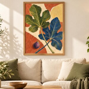 May include: A framed wall art print featuring a large green fig leaf and a large blue fig leaf overlapping on a background of abstract terracotta and cream shapes, with a single small purple fig fruit positioned in the lower left corner.