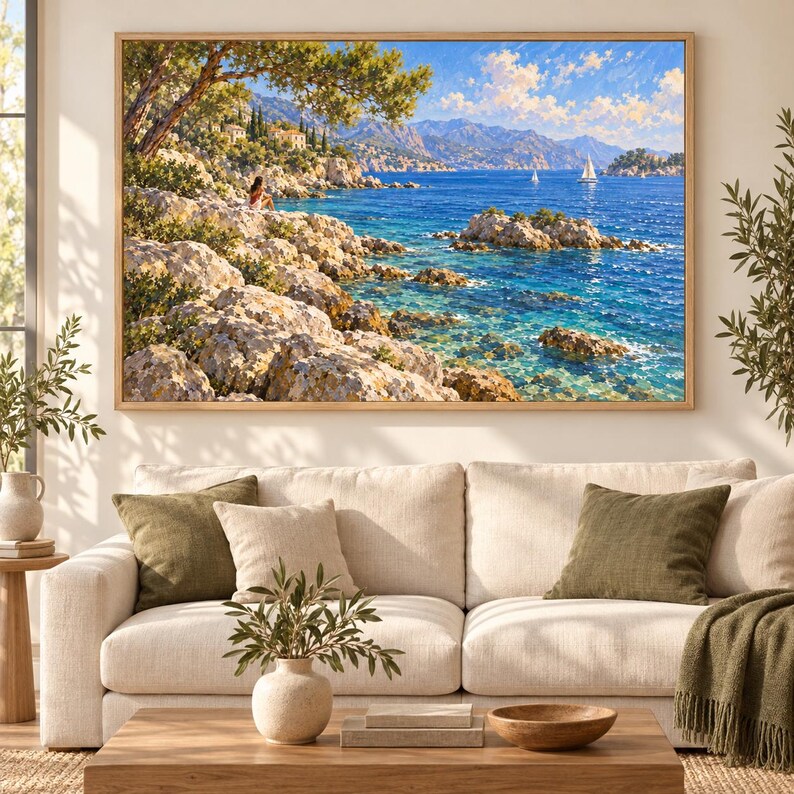 May include: A rectangular landscape painting in a light wood frame depicting a rocky Mediterranean coastline with a person sitting on the shore, turquoise water, distant mountains, and sailboats under a bright blue sky with scattered white clouds.