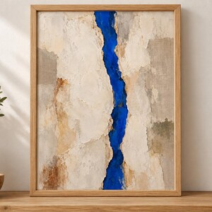 May include: A framed abstract wall art piece featuring a vertical, jagged fissure of vibrant cobalt blue running through the center of a textured, neutral-toned composition of beige, cream, and light brown layers within a light wood frame.