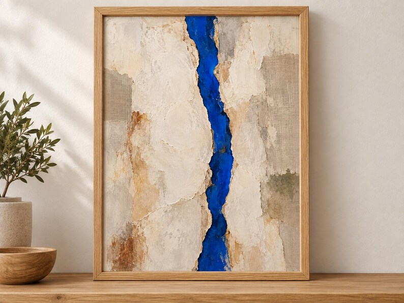 May include: A framed abstract wall art piece featuring a vertical, jagged fissure of vibrant cobalt blue running through the center of a textured, neutral-toned composition of beige, cream, and light brown layers within a light wood frame.