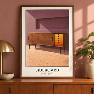 May include: A framed wall art print featuring a wooden sideboard with sliding doors and a column of five drawers in a gradient of yellow to orange. The text SIDEBOARD and Finn Juhl is printed in black at the bottom of the white matting.