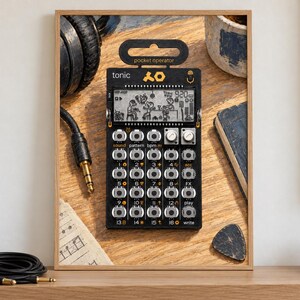May include: A black Teenage Engineering PO-32 Tonic pocket operator synthesizer featuring a monochrome LCD screen with animated graphics, a grid of sixteen circular buttons, two silver knobs, and the text pocket operator and tonic printed on the face.