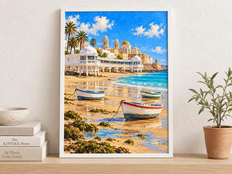 Op de afbeelding: Een ingelijste kunstdruk met een kusttafereel met drie kleine houten boten op een zandstrand. Op de achtergrond staat een witte kustpromenade met koepelvormige structuren en een kathedraal onder een helderblauwe lucht met wolken.