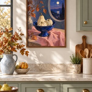 May include: A framed wall art print depicting a still life scene with three white pumpkins in a deep blue pedestal bowl, resting on a pink cloth. The background shows a circular window view of a moonlit sea, cypress trees, and autumn leaves.