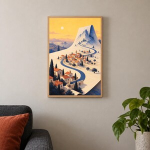 May include: A framed vertical art print depicting a Mediterranean-style village with terracotta-roofed buildings nestled at the base of a snow-capped mountain. A winding blue road leads through the town toward the peak under a warm yellow sky.