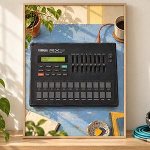 Pode incluir: Uma caixa de ritmos digital Yamaha RX11 preta com um ecr&atilde; LCD verde que mostra "SONG 01 J=120", v&aacute;rios bot&otilde;es quadrados cinzentos e cursores de volume verticais, apresentada como uma impress&atilde;o emoldurada com um fundo azul texturado.