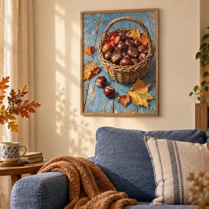 May include: A framed wall art print depicting a woven wicker basket filled with brown chestnuts, resting on a weathered blue wooden surface scattered with fallen autumn leaves in shades of yellow, orange, and brown, captured in a realistic style.