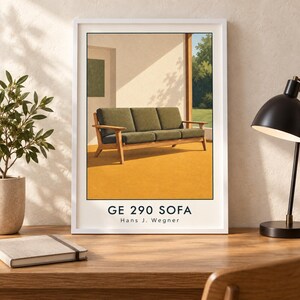 May include: A framed art print featuring a GE 290 sofa by Hans J. Wegner. The illustration depicts a wooden sofa with olive green cushions on a bright yellow floor, set against a sunlit interior with a view of trees through a large window.