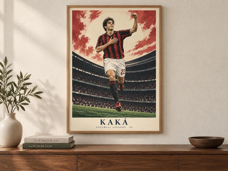 May include: A framed poster featuring a soccer player in a red and black striped jersey and white shorts, celebrating on a field with a stadium background. The text KAK&Aacute; and FOOTBALL LEGENDS 02 is printed at the bottom in a dark blue font.