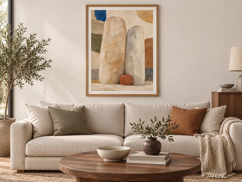 May include: A framed wall art print featuring an abstract composition of two large, vertical, stone-like shapes in beige and gray, accented by a small terracotta sphere at their base, set against a background of muted blue, green, and brown patches.