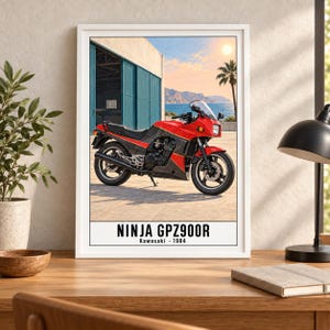 May include: A framed poster featuring a red and black 1984 Kawasaki Ninja GPZ900R motorcycle parked on a paved surface. The background shows a blue building, a palm tree, and a coastal landscape under a bright sun. The text reads NINJA GPZ900R Kawasaki 1984.