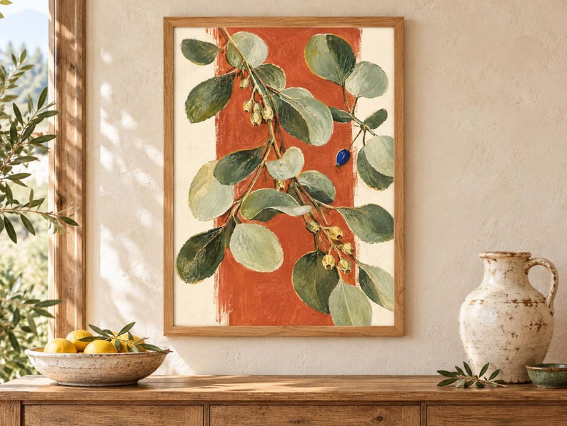 May include: A framed wall art print featuring a botanical illustration of a leafy branch with green foliage, small pale yellow buds, and a single dark blue berry, set against a vertical terracotta orange brushstroke on a cream background.