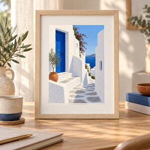 Puede incluir: Una l&aacute;mina enmarcada que muestra una escena mediterr&aacute;nea con edificios de piedra blanca, una puerta azul brillante, un olivo en maceta y flores de buganvilla de color rosa intenso. El camino conduce hacia un mar azul bajo un cielo despejado.