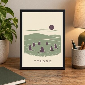 May include: A framed art print featuring a stylized landscape with a circle of standing stones in a green field, rolling hills, and a dark purple sun against a cream background. The word TYRONE is printed in black capital letters at the bottom.