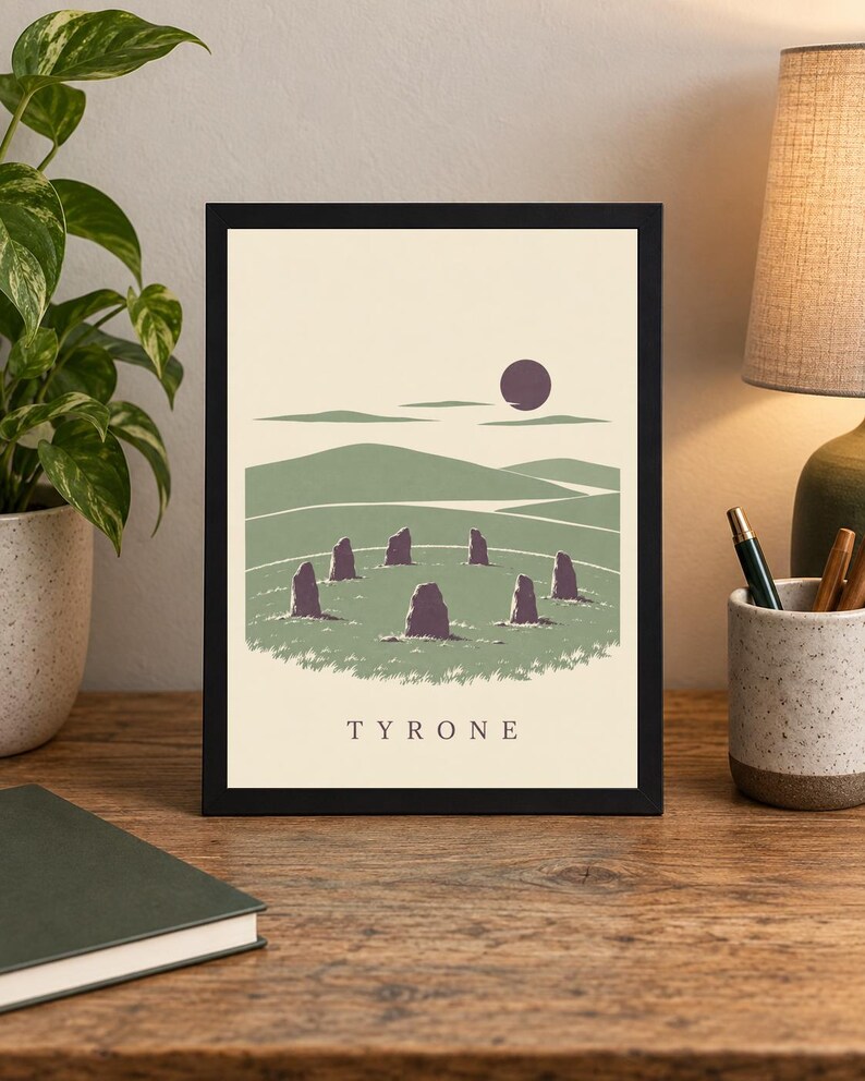 May include: A framed art print featuring a stylized landscape with a circle of standing stones in a green field, rolling hills, and a dark purple sun against a cream background. The word TYRONE is printed in black capital letters at the bottom.