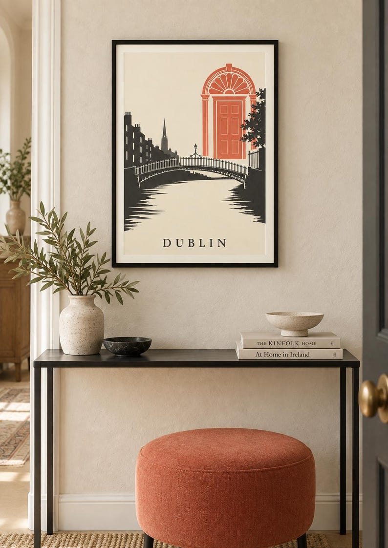 K&ouml;nnte beinhalten: Ein gerahmter Wandkunstdruck mit einer stilisierten Illustration von Dublin, Irland. Die Grafik zeigt eine schwarze Silhouette einer Br&uuml;cke und einer Skyline vor cremefarbenem Hintergrund, mit einer markanten orangefarbenen T&uuml;r und dem Text DUBLIN.