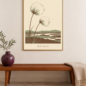 May include: A rectangular wall art print in a gold frame featuring a landscape illustration with two large, fluffy, dandelion-like seed heads in the foreground, green hills, and brown marshy terrain, with the word OFFALY printed at the bottom.