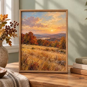 May include: A framed landscape painting depicting an autumn sunset over a rolling field of golden grass, with vibrant orange and red trees in the distance, a calm lake, and a soft, cloud-filled sky in shades of yellow, orange, and light blue.