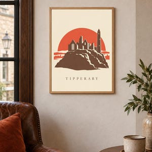 May include: A framed wall art print featuring a stylized illustration of the Rock of Cashel in Tipperary, Ireland. The design shows a brown silhouette of the stone ruins against a large, solid red sun on a cream background, with the text TIPPERARY.