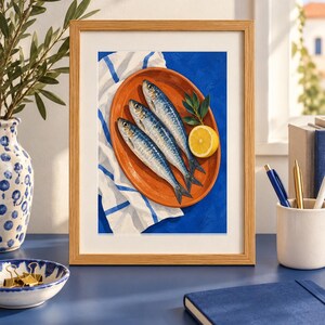 K&ouml;nnte beinhalten: Ein gerahmter Kunstdruck mit einem Gem&auml;lde von drei silbernen Sardinen auf einem ovalen, terrakottafarbenen Teller. Der Teller liegt auf einem wei&szlig;en Tuch mit blauen Streifen vor einem leuchtend blauen Hintergrund, erg&auml;nzt durch eine Zitronenscheibe und gr&uuml;ne Bl&auml;tter.