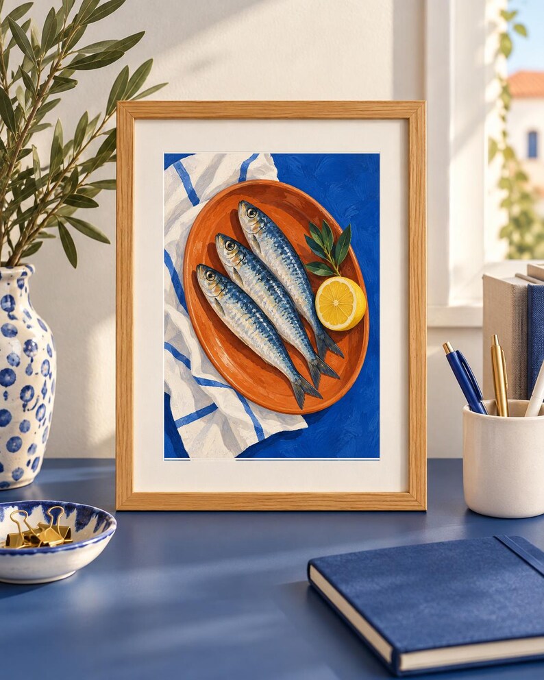 K&ouml;nnte beinhalten: Ein gerahmter Kunstdruck mit einem Gem&auml;lde von drei silbernen Sardinen auf einem ovalen, terrakottafarbenen Teller. Der Teller liegt auf einem wei&szlig;en Tuch mit blauen Streifen vor einem leuchtend blauen Hintergrund, erg&auml;nzt durch eine Zitronenscheibe und gr&uuml;ne Bl&auml;tter.